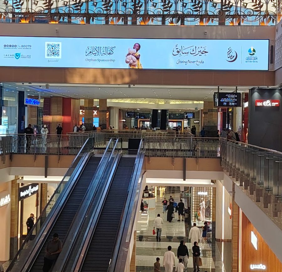 شاشة طويلة فوق السلالم المتحركة في بهو مول تعرض إعلان جمعية دار البر